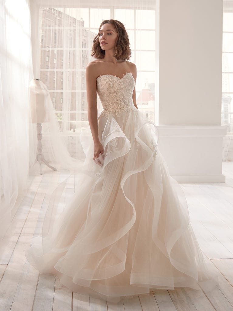 Romantic mermaid wedding dress of light pink Chantilly lace with plunging V-neck that continues on the sleeves. The keyhole opening in back and the tulle overskirt add romanticism to this dreamy dress.
