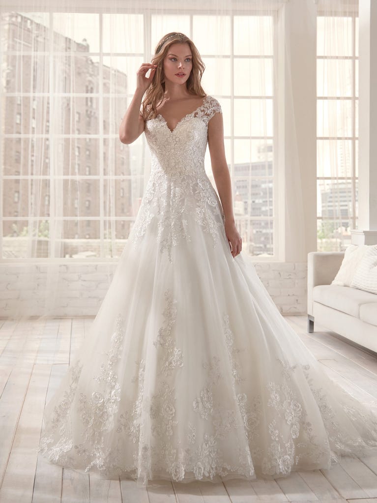 Romantic mermaid wedding dress of light pink Chantilly lace with plunging V-neck that continues on the sleeves. The keyhole opening in back and the tulle overskirt add romanticism to this dreamy dress.