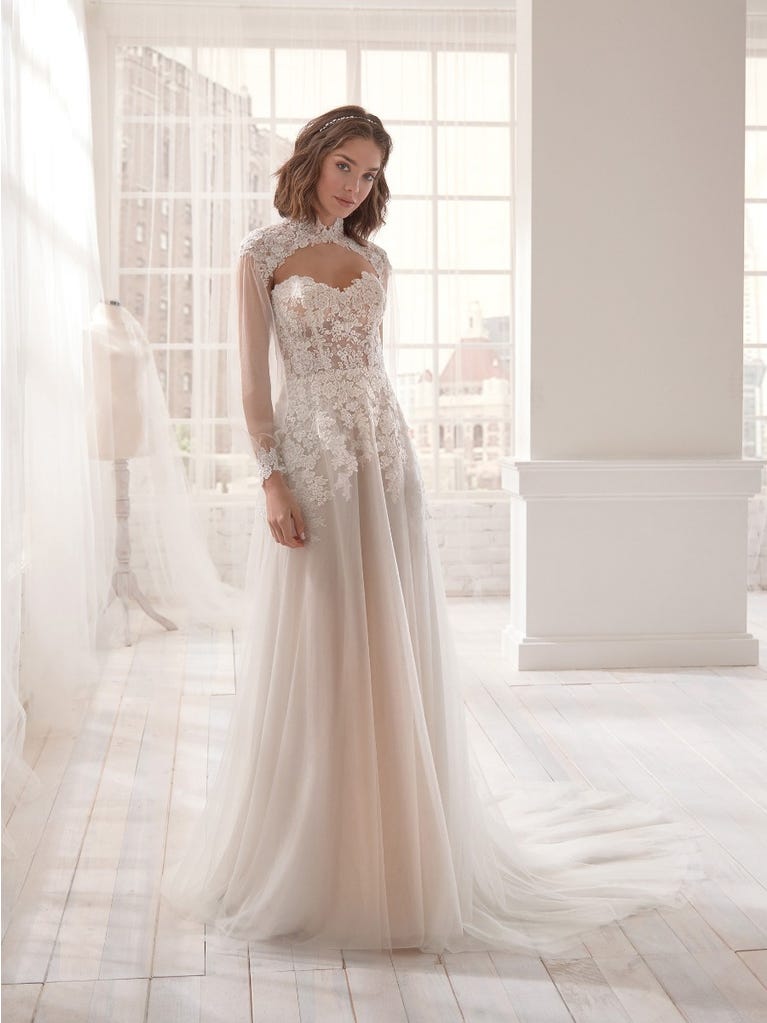 Romantic mermaid wedding dress of light pink Chantilly lace with plunging V-neck that continues on the sleeves. The keyhole opening in back and the tulle overskirt add romanticism to this dreamy dress.
