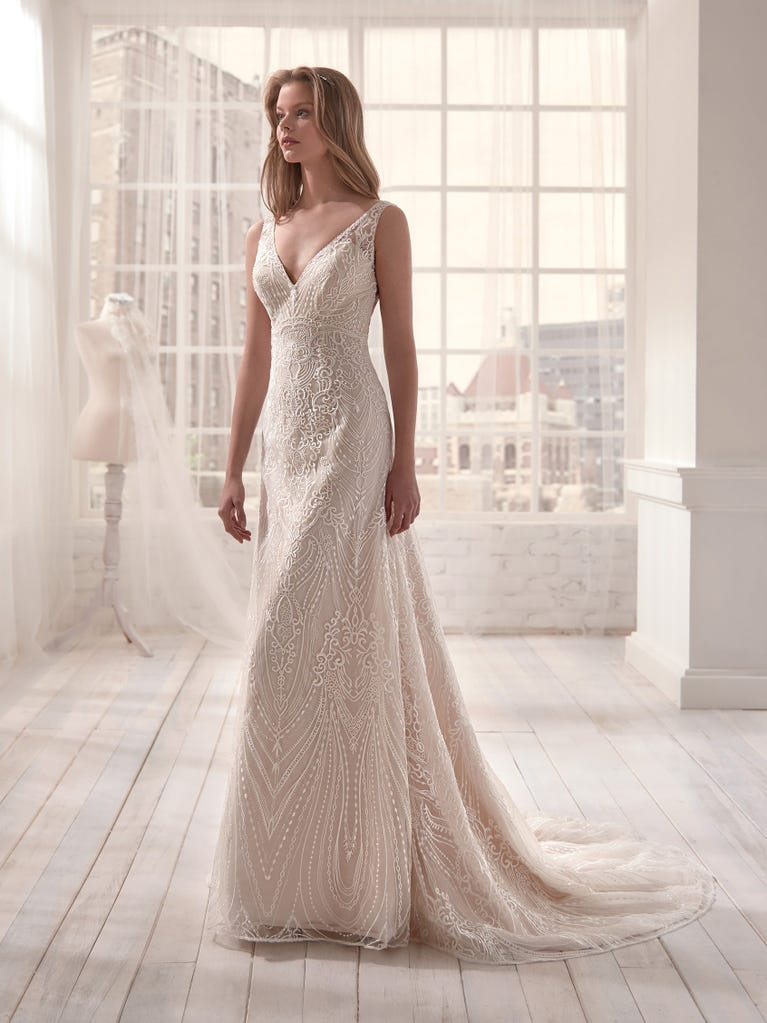 Romantic mermaid wedding dress of light pink Chantilly lace with plunging V-neck that continues on the sleeves. The keyhole opening in back and the tulle overskirt add romanticism to this dreamy dress.