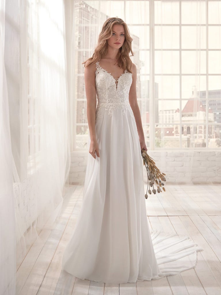 Romantic mermaid wedding dress of light pink Chantilly lace with plunging V-neck that continues on the sleeves. The keyhole opening in back and the tulle overskirt add romanticism to this dreamy dress.