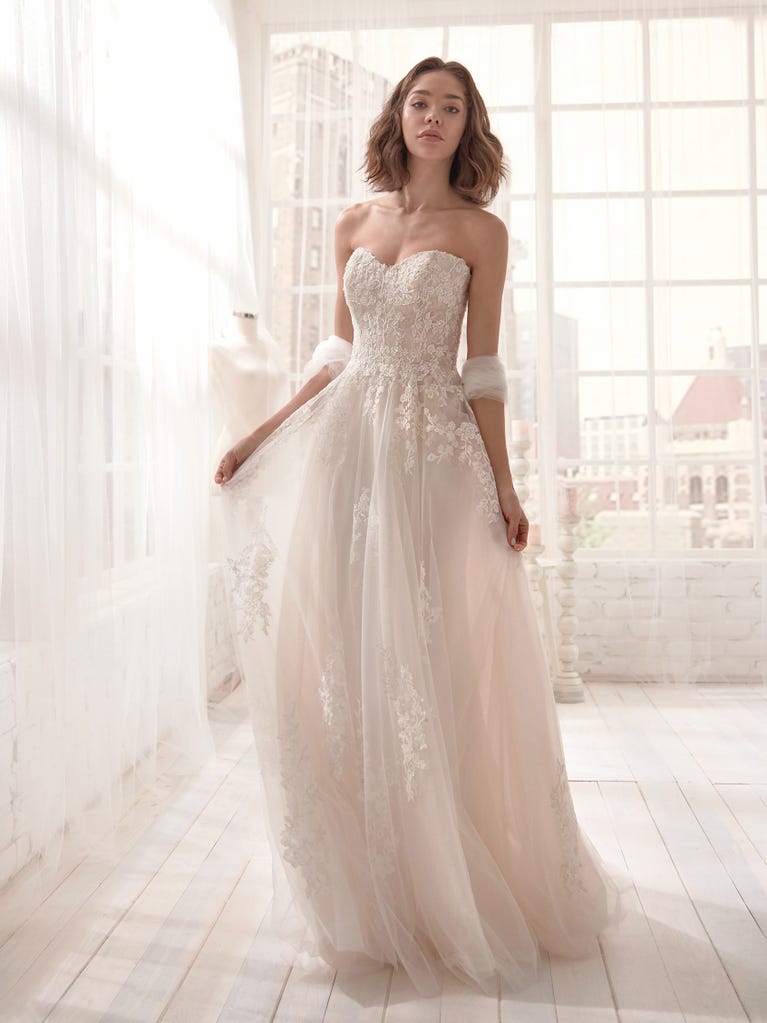 Romantic mermaid wedding dress of light pink Chantilly lace with plunging V-neck that continues on the sleeves. The keyhole opening in back and the tulle overskirt add romanticism to this dreamy dress.