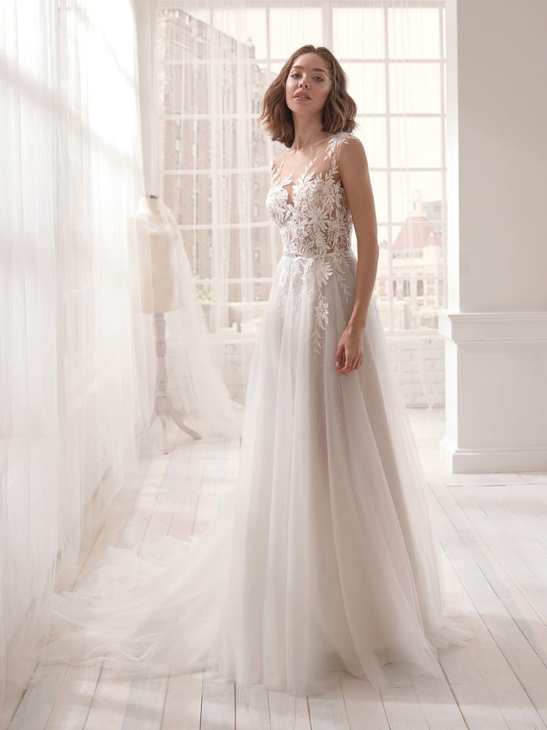 Romantic mermaid wedding dress of light pink Chantilly lace with plunging V-neck that continues on the sleeves. The keyhole opening in back and the tulle overskirt add romanticism to this dreamy dress.