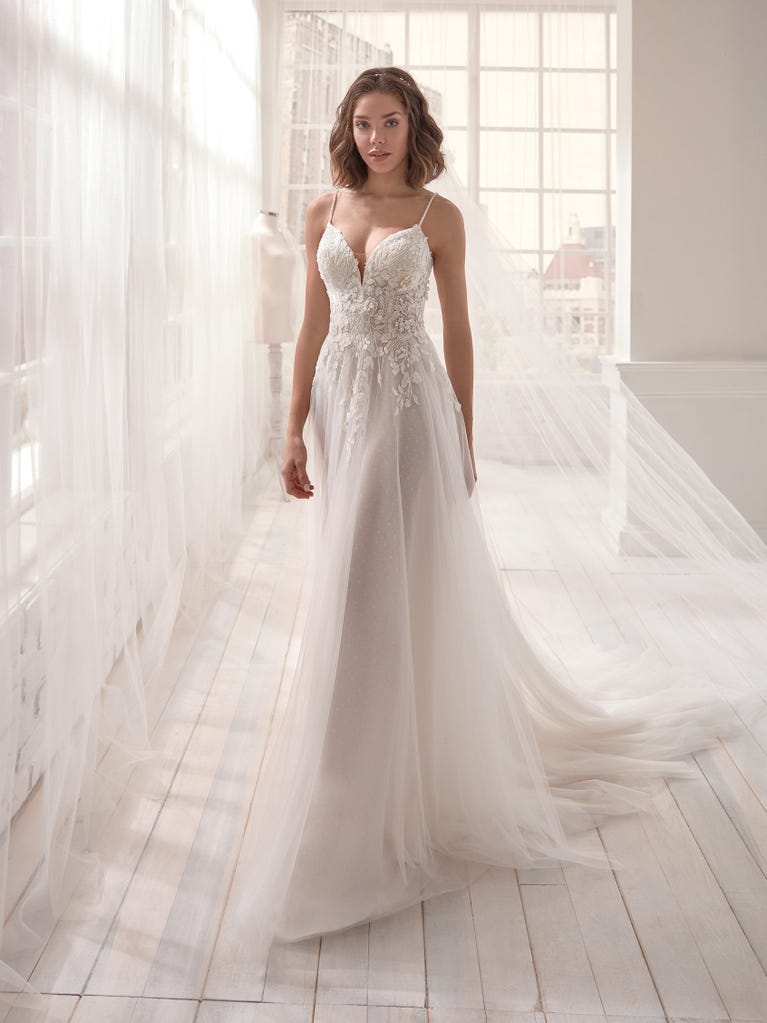 Romantic mermaid wedding dress of light pink Chantilly lace with plunging V-neck that continues on the sleeves. The keyhole opening in back and the tulle overskirt add romanticism to this dreamy dress.