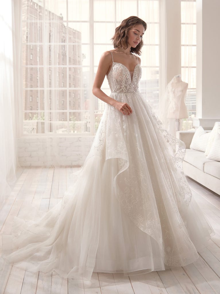 Romantic mermaid wedding dress of light pink Chantilly lace with plunging V-neck that continues on the sleeves. The keyhole opening in back and the tulle overskirt add romanticism to this dreamy dress.