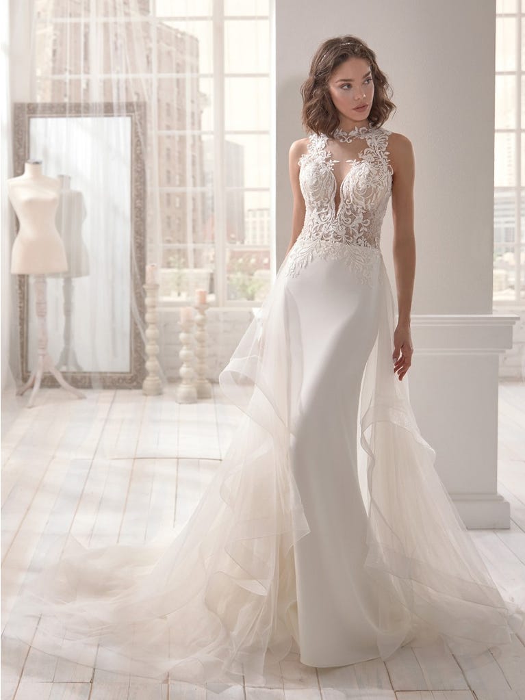 Romantic mermaid wedding dress of light pink Chantilly lace with plunging V-neck that continues on the sleeves. The keyhole opening in back and the tulle overskirt add romanticism to this dreamy dress.