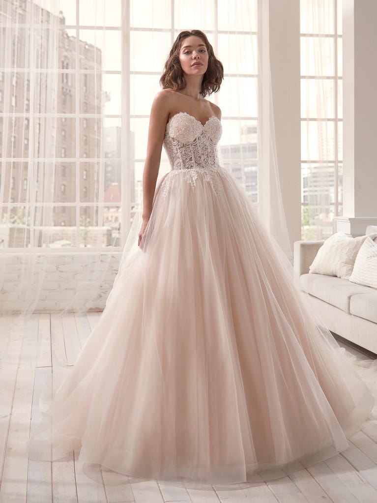 Romantic mermaid wedding dress of light pink Chantilly lace with plunging V-neck that continues on the sleeves. The keyhole opening in back and the tulle overskirt add romanticism to this dreamy dress.