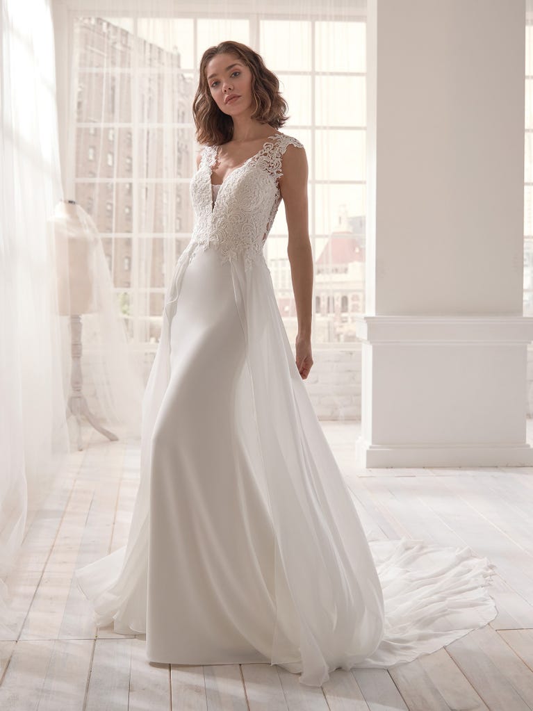 Romantic mermaid wedding dress of light pink Chantilly lace with plunging V-neck that continues on the sleeves. The keyhole opening in back and the tulle overskirt add romanticism to this dreamy dress.