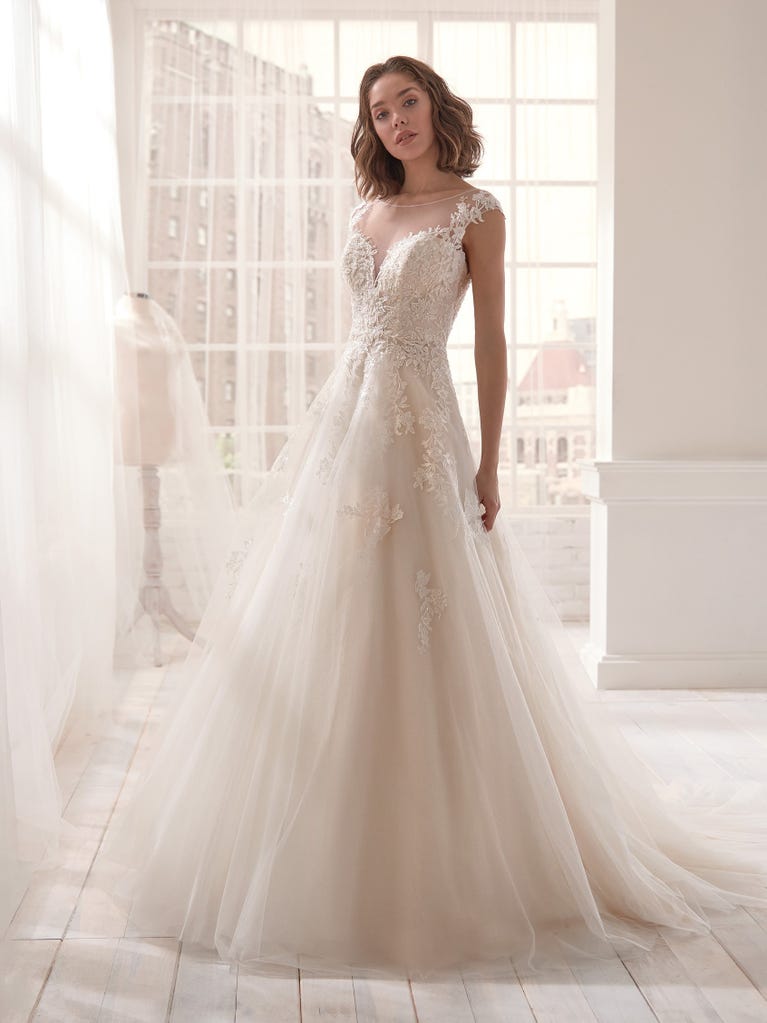 Romantic mermaid wedding dress of light pink Chantilly lace with plunging V-neck that continues on the sleeves. The keyhole opening in back and the tulle overskirt add romanticism to this dreamy dress.