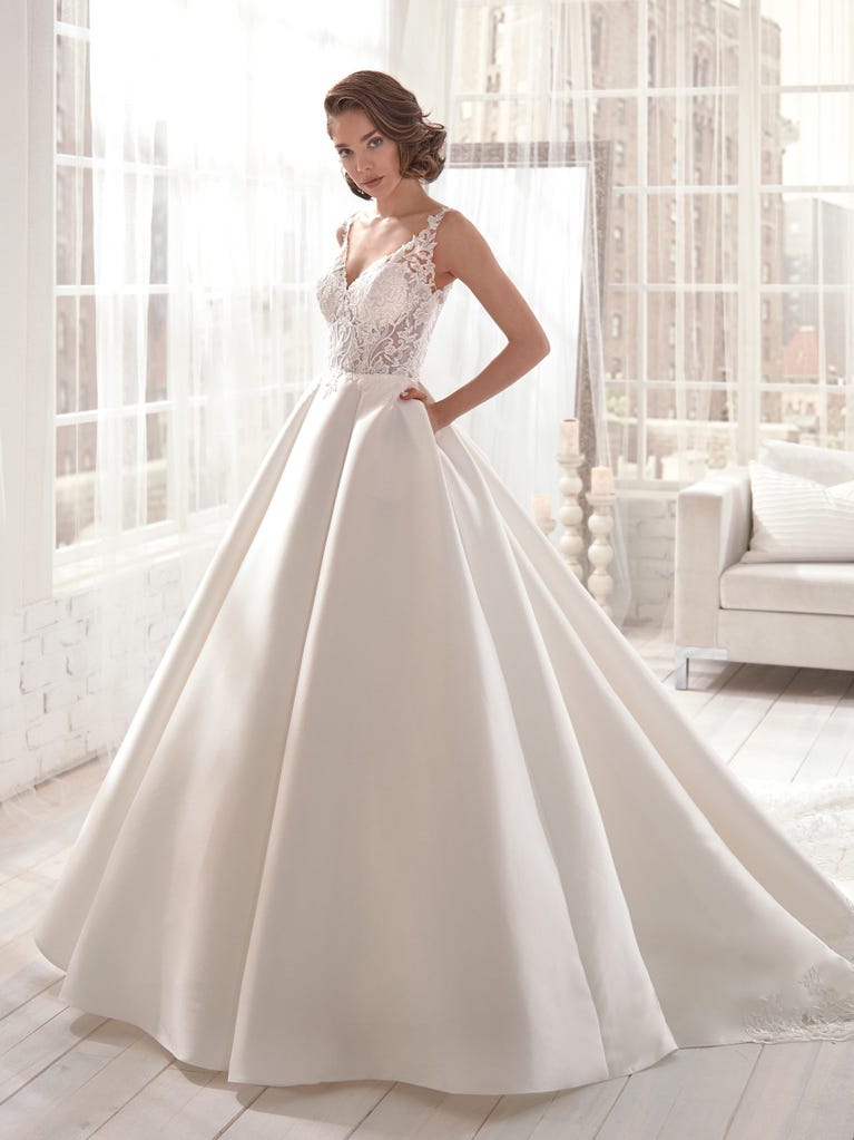 Romantic mermaid wedding dress of light pink Chantilly lace with plunging V-neck that continues on the sleeves. The keyhole opening in back and the tulle overskirt add romanticism to this dreamy dress.
