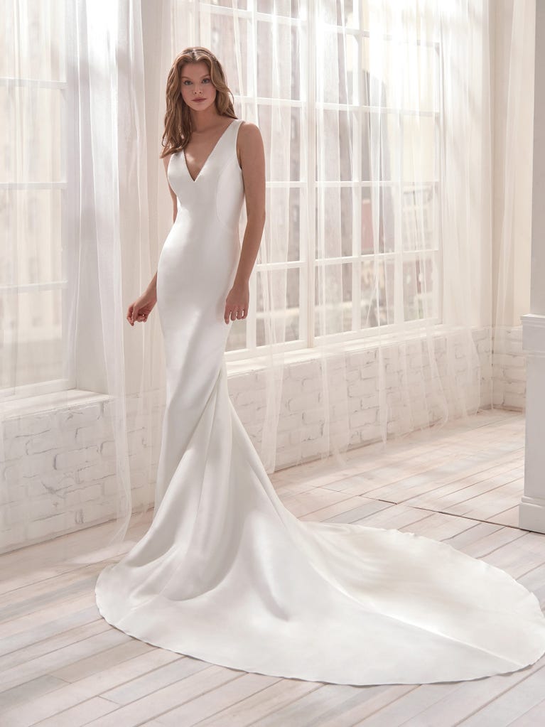 Romantic mermaid wedding dress of light pink Chantilly lace with plunging V-neck that continues on the sleeves. The keyhole opening in back and the tulle overskirt add romanticism to this dreamy dress.