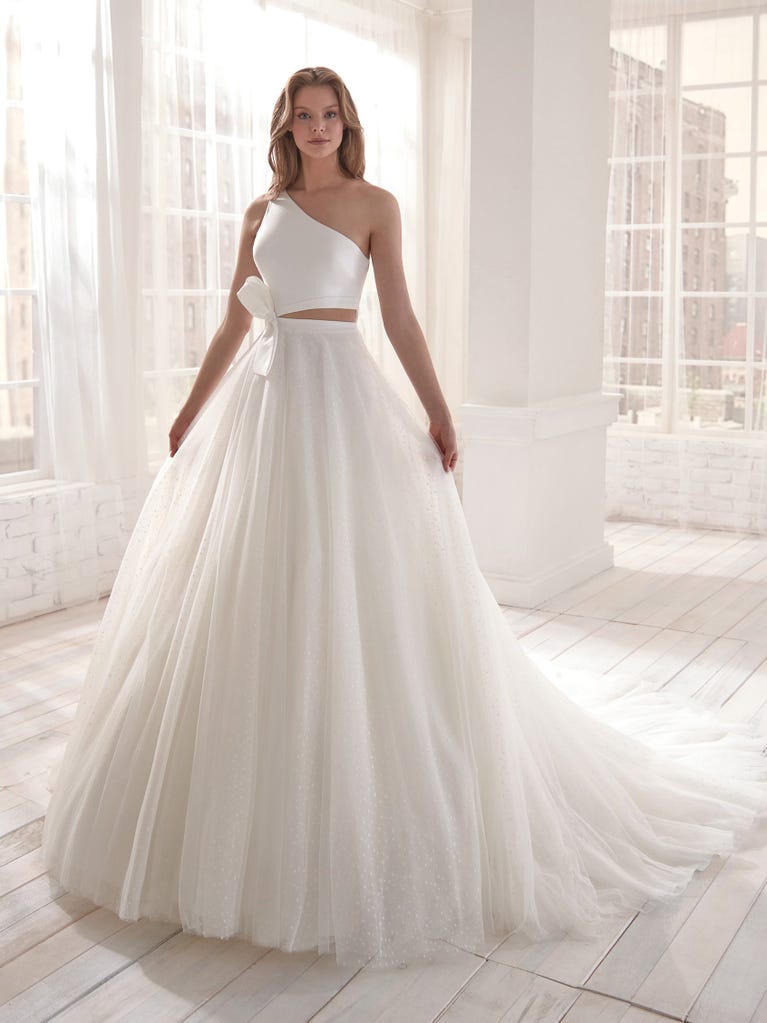 Romantic mermaid wedding dress of light pink Chantilly lace with plunging V-neck that continues on the sleeves. The keyhole opening in back and the tulle overskirt add romanticism to this dreamy dress.