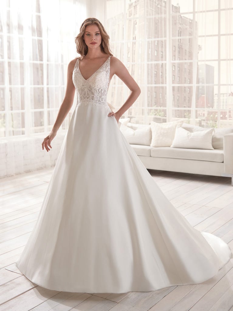Romantic mermaid wedding dress of light pink Chantilly lace with plunging V-neck that continues on the sleeves. The keyhole opening in back and the tulle overskirt add romanticism to this dreamy dress.