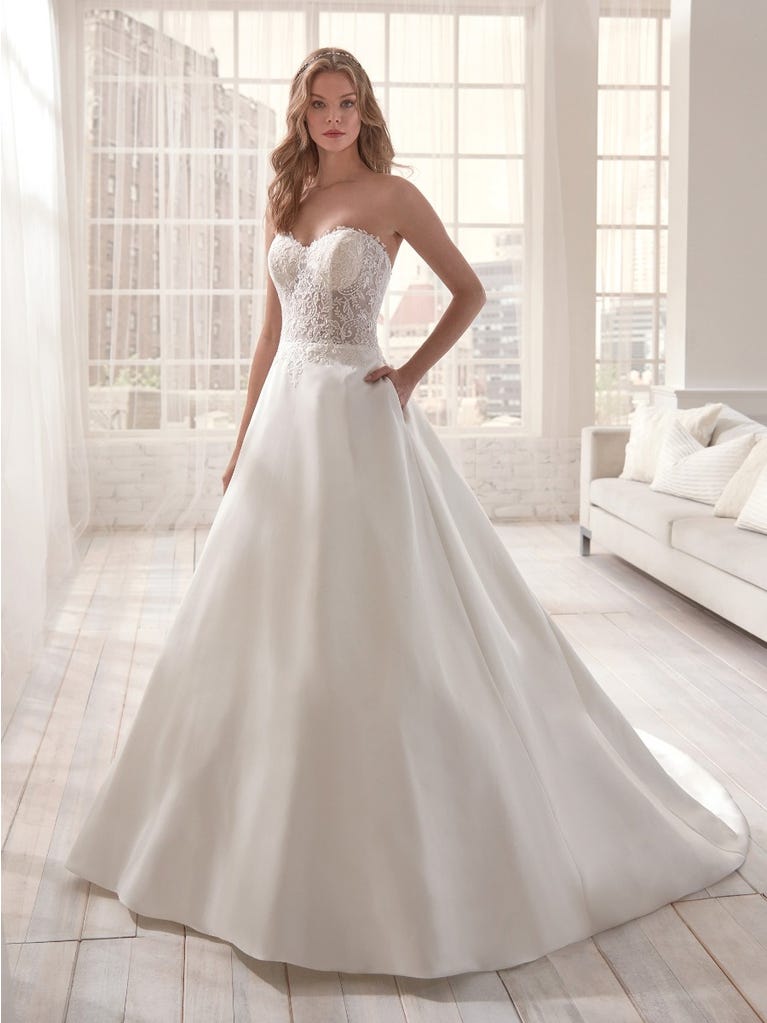 Romantic mermaid wedding dress of light pink Chantilly lace with plunging V-neck that continues on the sleeves. The keyhole opening in back and the tulle overskirt add romanticism to this dreamy dress.