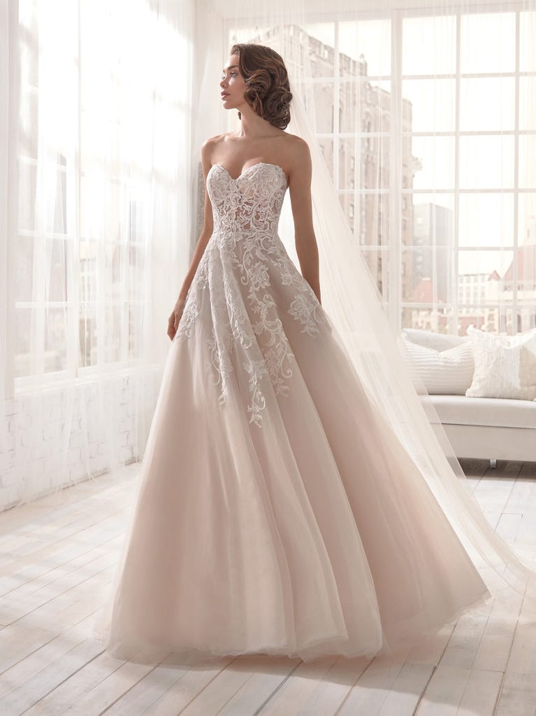 Romantic mermaid wedding dress of light pink Chantilly lace with plunging V-neck that continues on the sleeves. The keyhole opening in back and the tulle overskirt add romanticism to this dreamy dress.