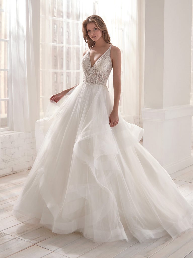 Romantic mermaid wedding dress of light pink Chantilly lace with plunging V-neck that continues on the sleeves. The keyhole opening in back and the tulle overskirt add romanticism to this dreamy dress.