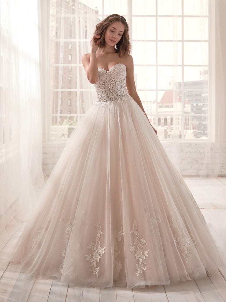 Romantic mermaid wedding dress of light pink Chantilly lace with plunging V-neck that continues on the sleeves. The keyhole opening in back and the tulle overskirt add romanticism to this dreamy dress.