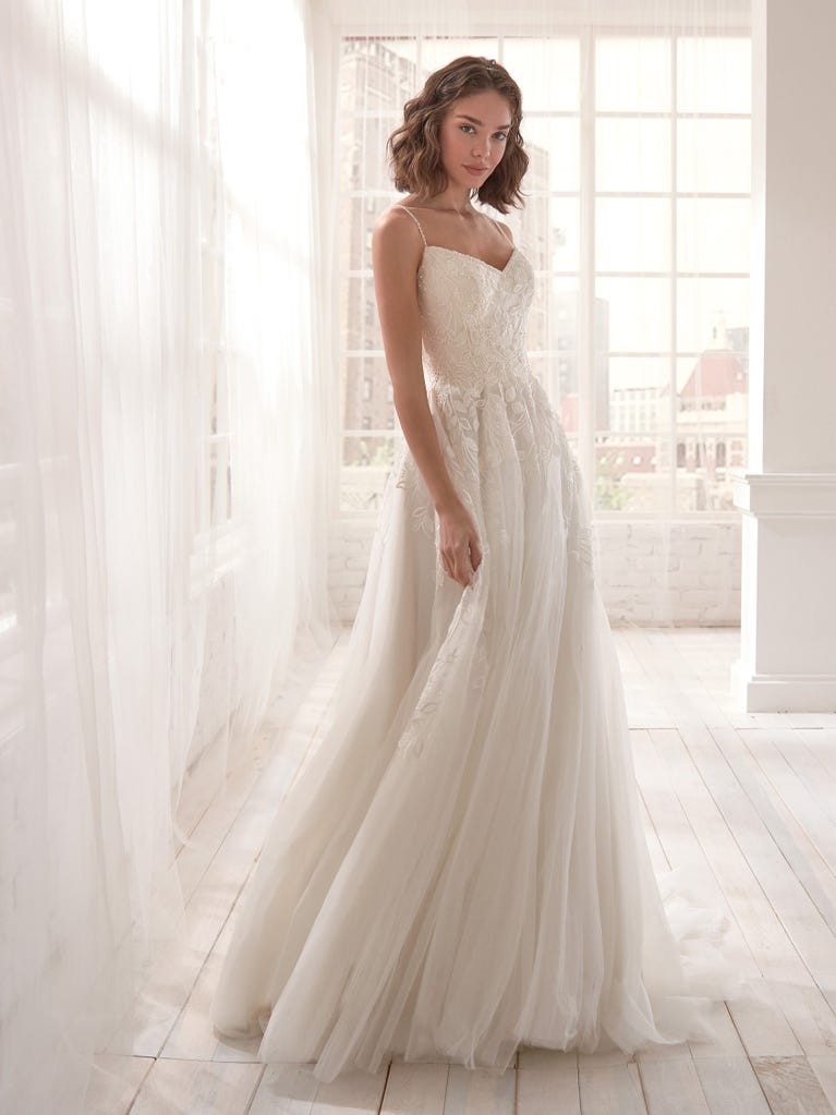 Romantic mermaid wedding dress of light pink Chantilly lace with plunging V-neck that continues on the sleeves. The keyhole opening in back and the tulle overskirt add romanticism to this dreamy dress.