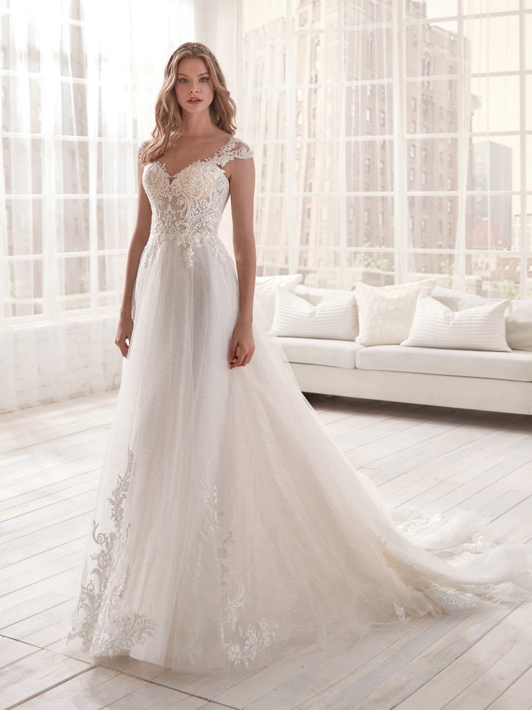 Romantic mermaid wedding dress of light pink Chantilly lace with plunging V-neck that continues on the sleeves. The keyhole opening in back and the tulle overskirt add romanticism to this dreamy dress.