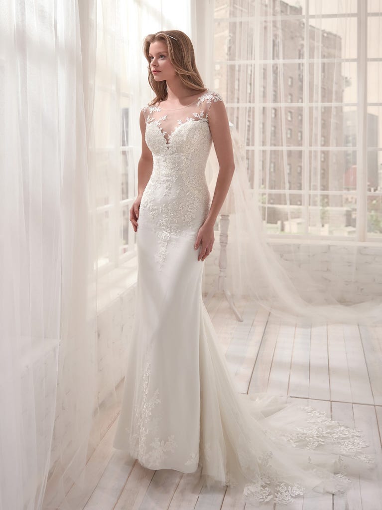 Romantic mermaid wedding dress of light pink Chantilly lace with plunging V-neck that continues on the sleeves. The keyhole opening in back and the tulle overskirt add romanticism to this dreamy dress.