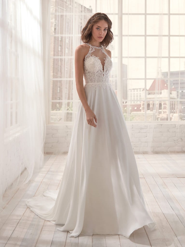 Romantic mermaid wedding dress of light pink Chantilly lace with plunging V-neck that continues on the sleeves. The keyhole opening in back and the tulle overskirt add romanticism to this dreamy dress.