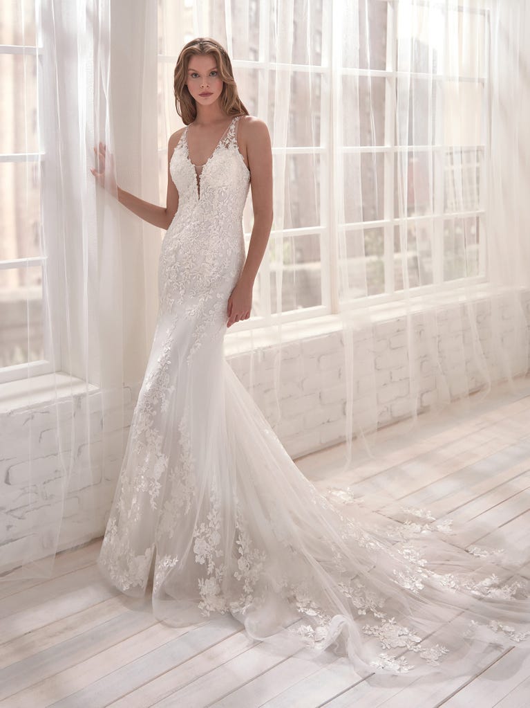 Romantic mermaid wedding dress of light pink Chantilly lace with plunging V-neck that continues on the sleeves. The keyhole opening in back and the tulle overskirt add romanticism to this dreamy dress.