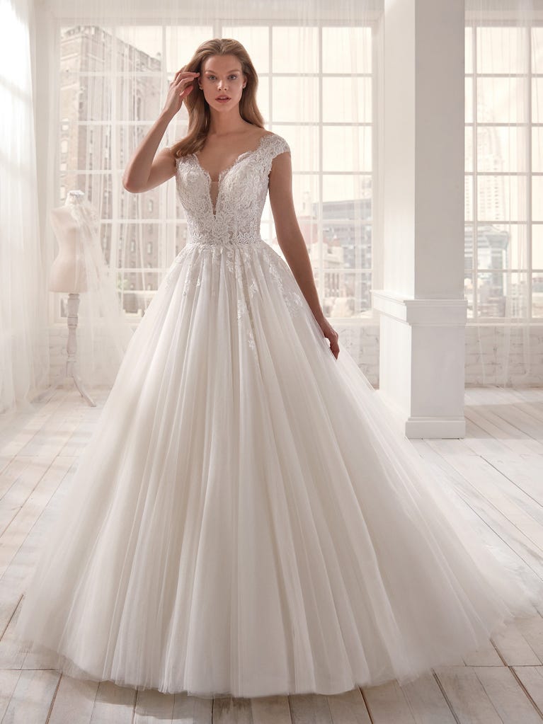 Romantic mermaid wedding dress of light pink Chantilly lace with plunging V-neck that continues on the sleeves. The keyhole opening in back and the tulle overskirt add romanticism to this dreamy dress.