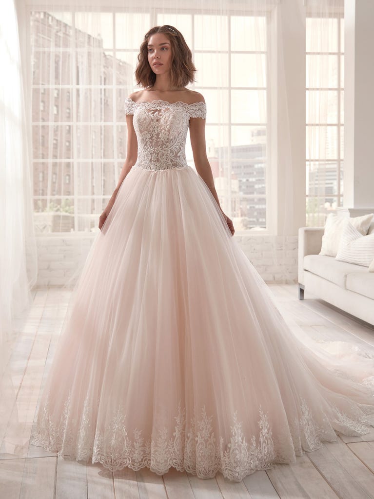 Romantic mermaid wedding dress of light pink Chantilly lace with plunging V-neck that continues on the sleeves. The keyhole opening in back and the tulle overskirt add romanticism to this dreamy dress.