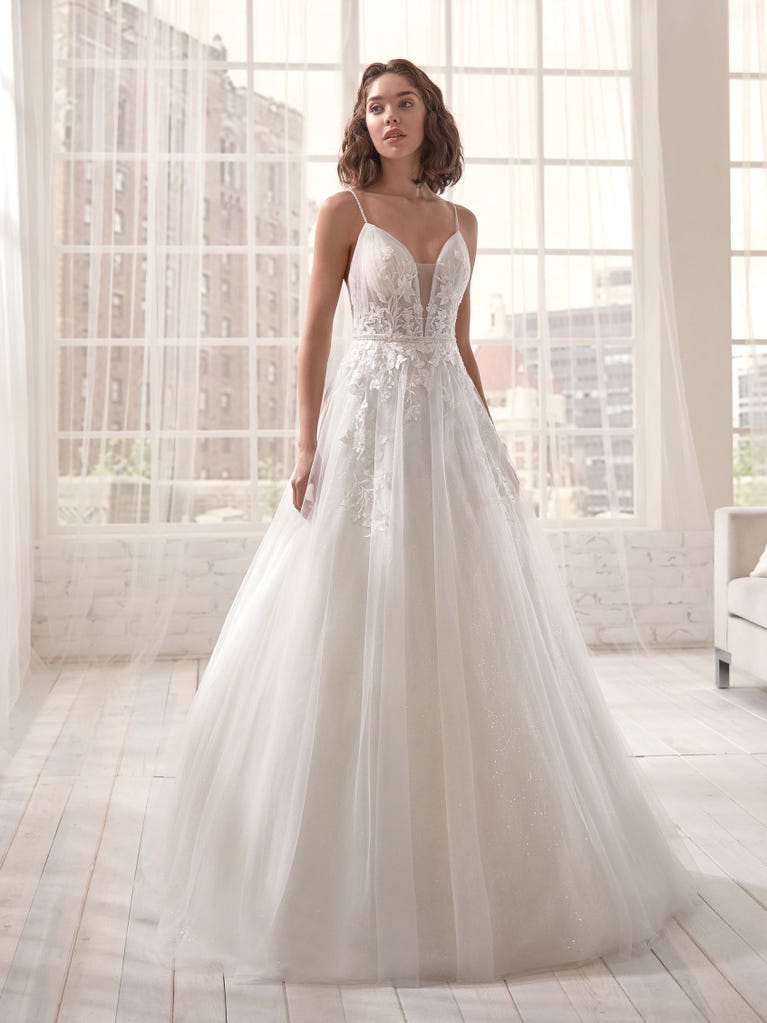 Romantic mermaid wedding dress of light pink Chantilly lace with plunging V-neck that continues on the sleeves. The keyhole opening in back and the tulle overskirt add romanticism to this dreamy dress.