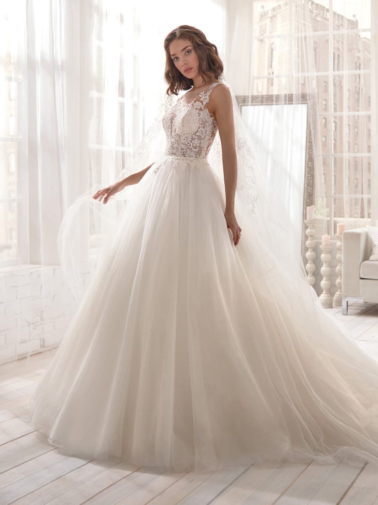 Romantic mermaid wedding dress of light pink Chantilly lace with plunging V-neck that continues on the sleeves. The keyhole opening in back and the tulle overskirt add romanticism to this dreamy dress.