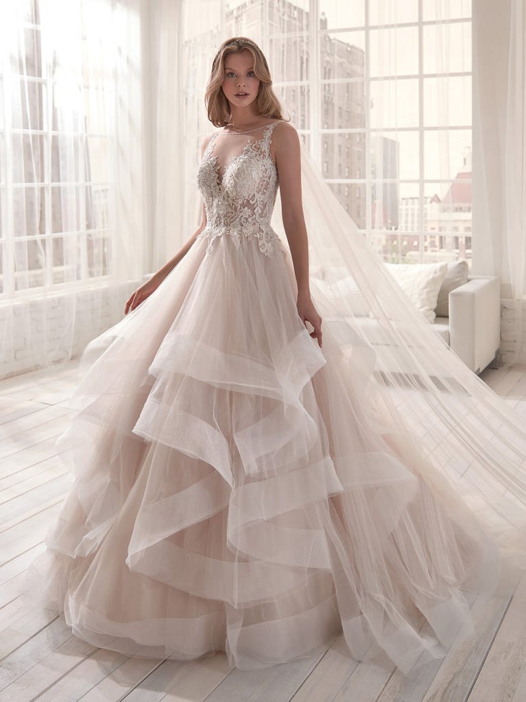 Romantic mermaid wedding dress of light pink Chantilly lace with plunging V-neck that continues on the sleeves. The keyhole opening in back and the tulle overskirt add romanticism to this dreamy dress.