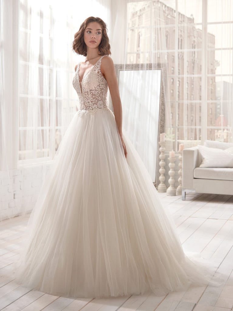 Romantic mermaid wedding dress of light pink Chantilly lace with plunging V-neck that continues on the sleeves. The keyhole opening in back and the tulle overskirt add romanticism to this dreamy dress.