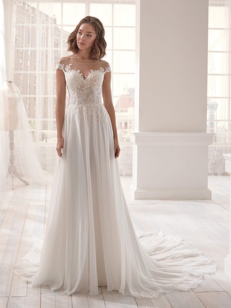 Romantic mermaid wedding dress of light pink Chantilly lace with plunging V-neck that continues on the sleeves. The keyhole opening in back and the tulle overskirt add romanticism to this dreamy dress.