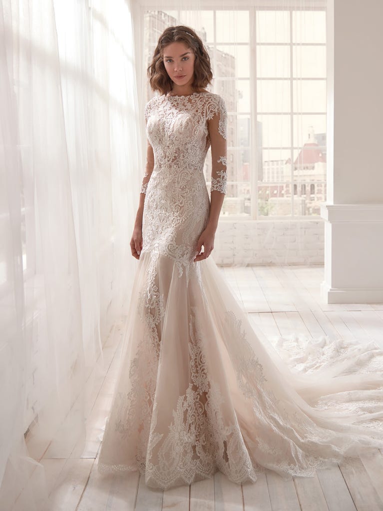 Romantic mermaid wedding dress of light pink Chantilly lace with plunging V-neck that continues on the sleeves. The keyhole opening in back and the tulle overskirt add romanticism to this dreamy dress.