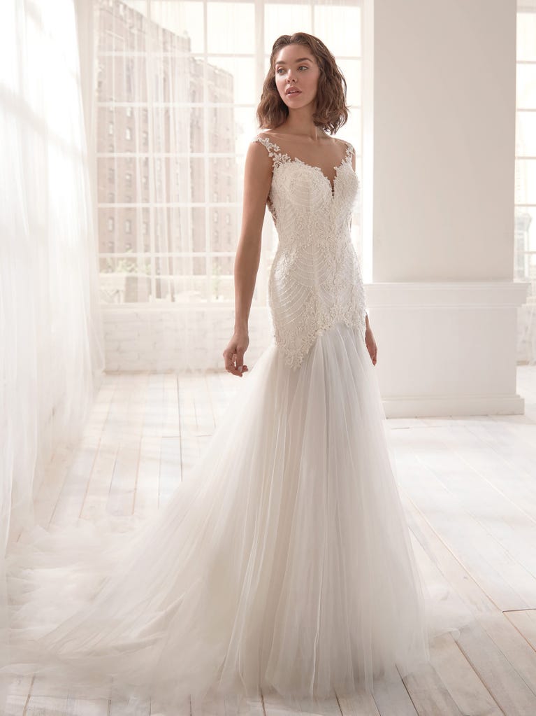 Romantic mermaid wedding dress of light pink Chantilly lace with plunging V-neck that continues on the sleeves. The keyhole opening in back and the tulle overskirt add romanticism to this dreamy dress.