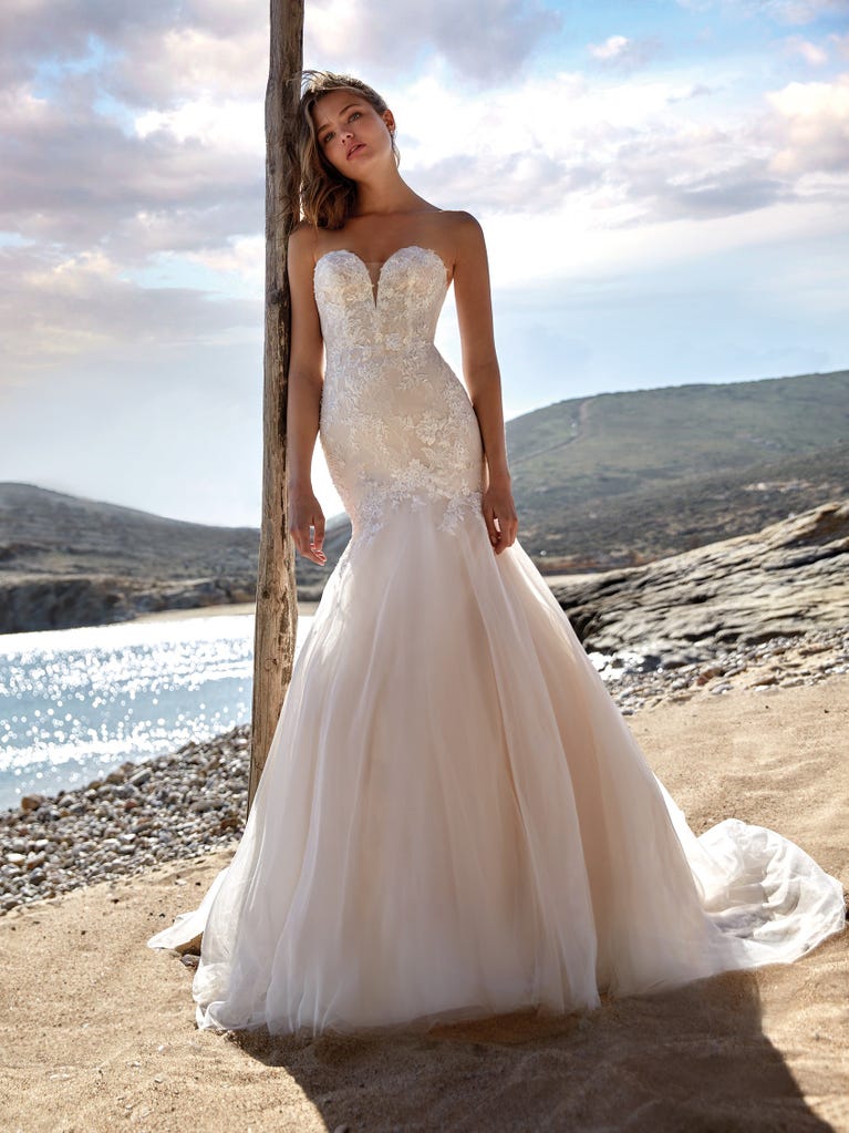 Flared wedding dress with crepe skirt and a tulle cape embroidered with silver beads. The three-dimensional flowers and minimalist, geometric superimpositions of fabrics create a contemporary, unique look for brides who want to surprise.