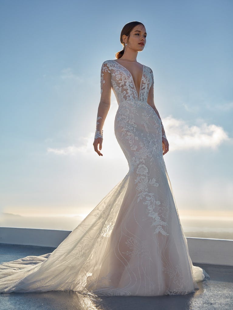 Flared wedding dress with crepe skirt and a tulle cape embroidered with silver beads. The three-dimensional flowers and minimalist, geometric superimpositions of fabrics create a contemporary, unique look for brides who want to surprise.