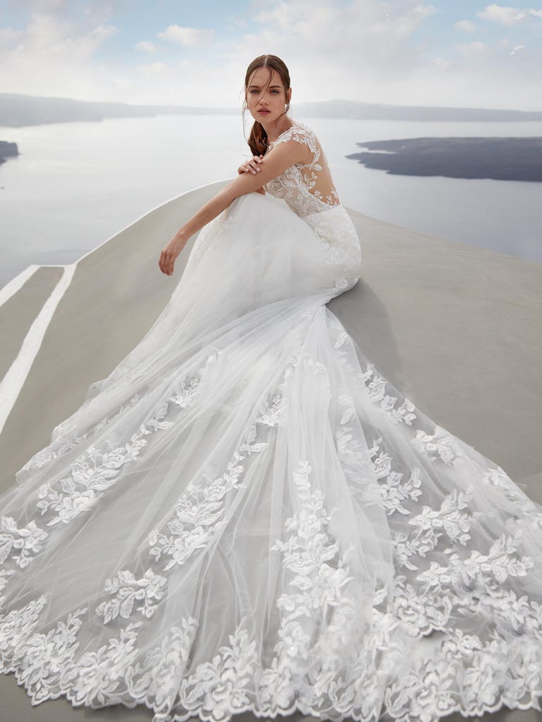 Flared wedding dress with crepe skirt and a tulle cape embroidered with silver beads. The three-dimensional flowers and minimalist, geometric superimpositions of fabrics create a contemporary, unique look for brides who want to surprise.