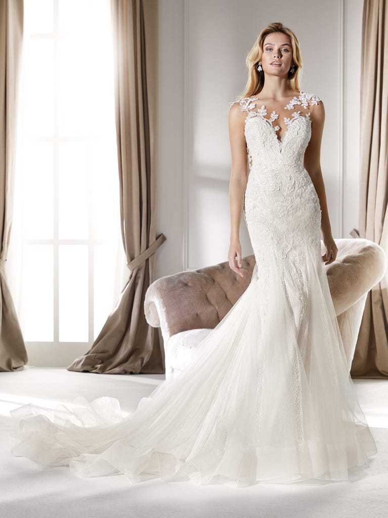 Romantic mermaid wedding dress of light pink Chantilly lace with plunging V-neck that continues on the sleeves. The keyhole opening in back and the tulle overskirt add romanticism to this dreamy dress.