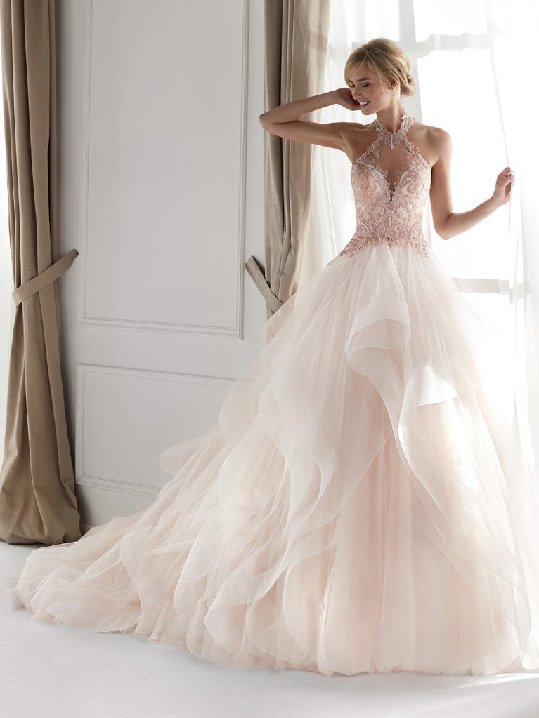 Romantic mermaid wedding dress of light pink Chantilly lace with plunging V-neck that continues on the sleeves. The keyhole opening in back and the tulle overskirt add romanticism to this dreamy dress.