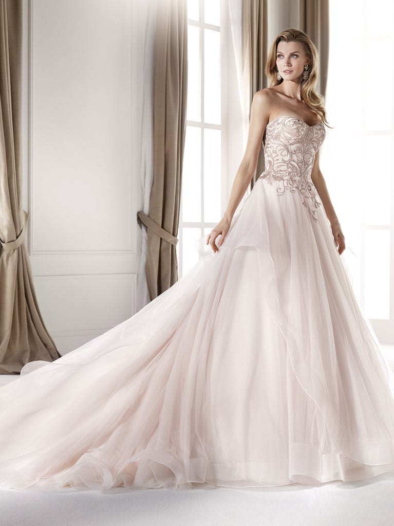Romantic mermaid wedding dress of light pink Chantilly lace with plunging V-neck that continues on the sleeves. The keyhole opening in back and the tulle overskirt add romanticism to this dreamy dress.