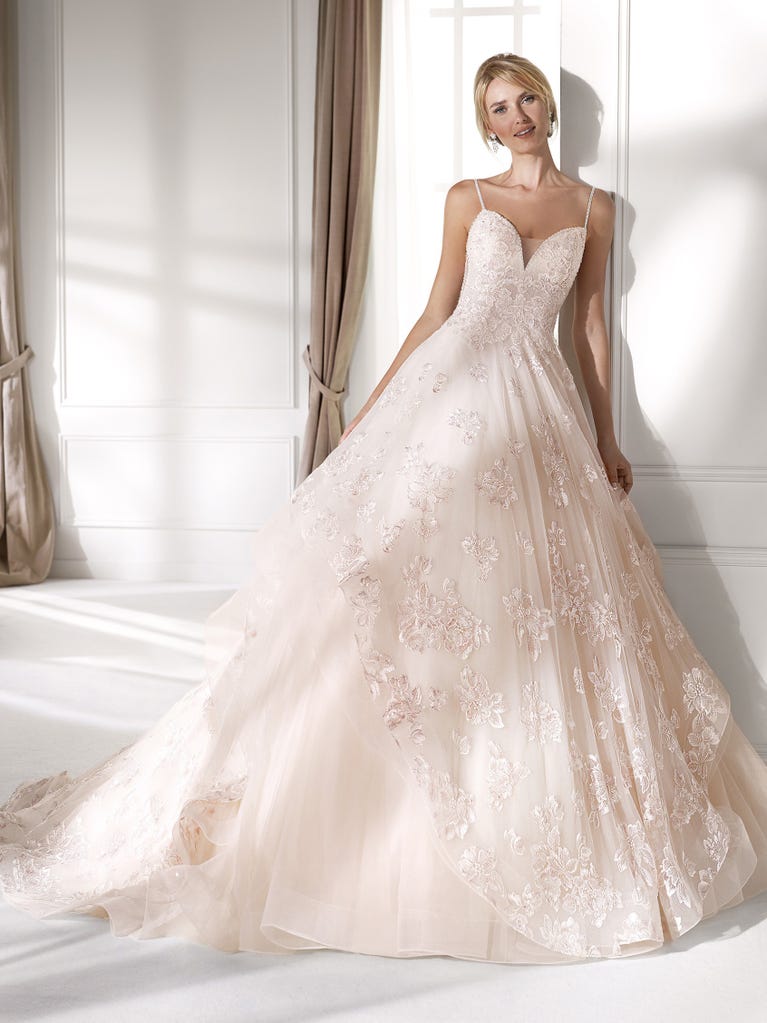 Romantic mermaid wedding dress of light pink Chantilly lace with plunging V-neck that continues on the sleeves. The keyhole opening in back and the tulle overskirt add romanticism to this dreamy dress.
