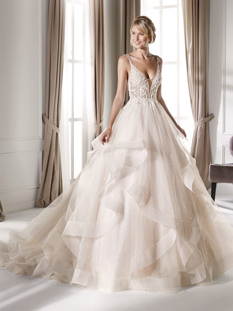 Romantic mermaid wedding dress of light pink Chantilly lace with plunging V-neck that continues on the sleeves. The keyhole opening in back and the tulle overskirt add romanticism to this dreamy dress.