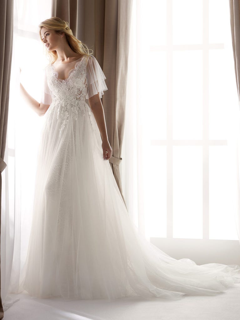 Fit & flare champagne tulle wedding dress with off-white guipure lace floral designs. The rounded neckline with tattoo-effect lace is highlighted with a refined, romantic 3D flower on the shoulder.