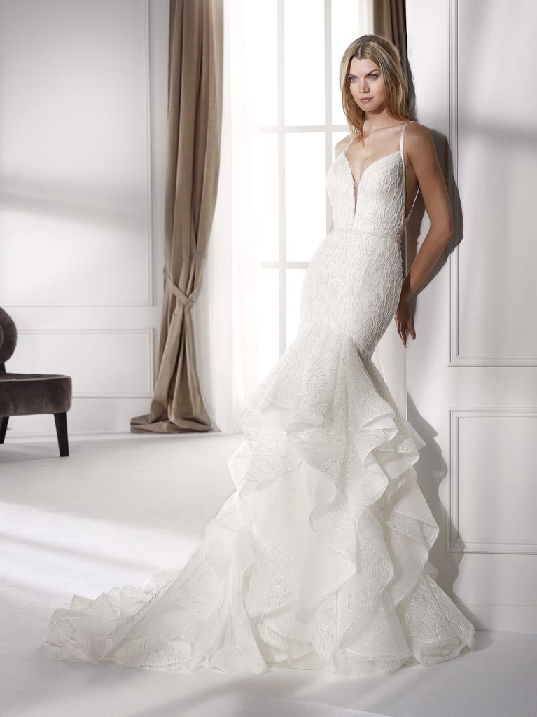 Romantic mermaid wedding dress of light pink Chantilly lace with plunging V-neck that continues on the sleeves. The keyhole opening in back and the tulle overskirt add romanticism to this dreamy dress.