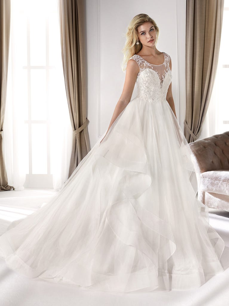 Romantic mermaid wedding dress of light pink Chantilly lace with plunging V-neck that continues on the sleeves. The keyhole opening in back and the tulle overskirt add romanticism to this dreamy dress.