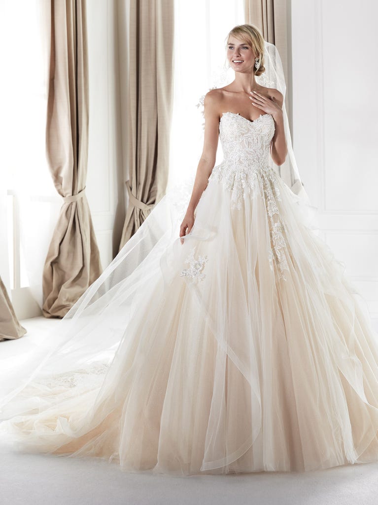 Romantic mermaid wedding dress of light pink Chantilly lace with plunging V-neck that continues on the sleeves. The keyhole opening in back and the tulle overskirt add romanticism to this dreamy dress.