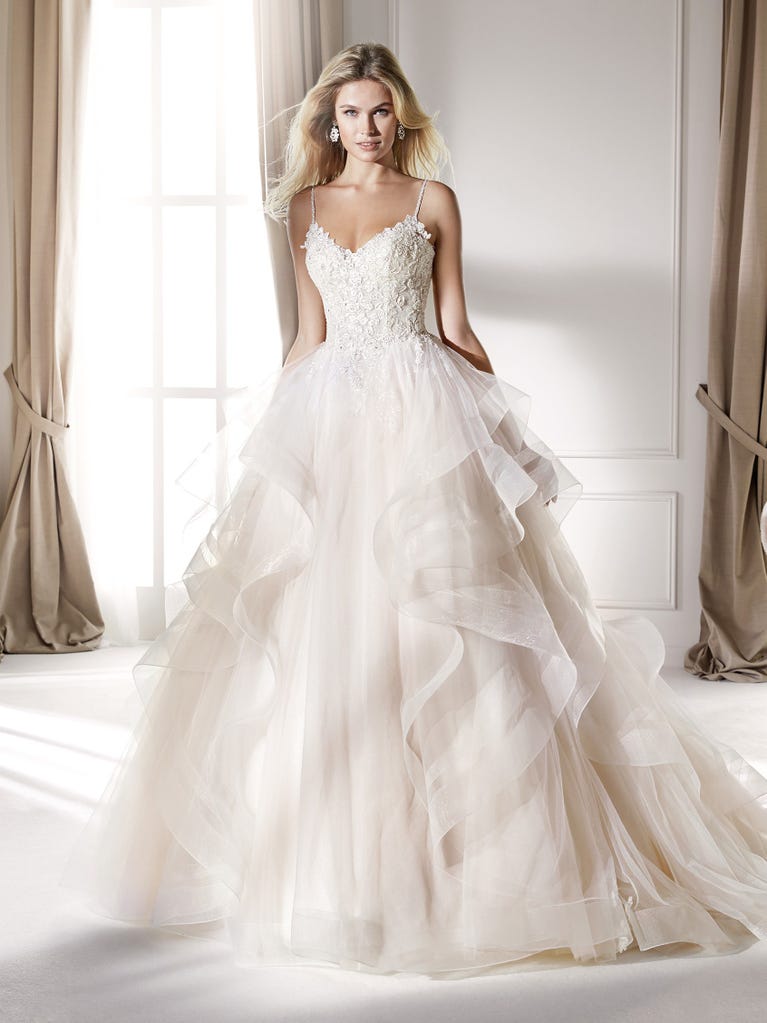 Romantic mermaid wedding dress of light pink Chantilly lace with plunging V-neck that continues on the sleeves. The keyhole opening in back and the tulle overskirt add romanticism to this dreamy dress.