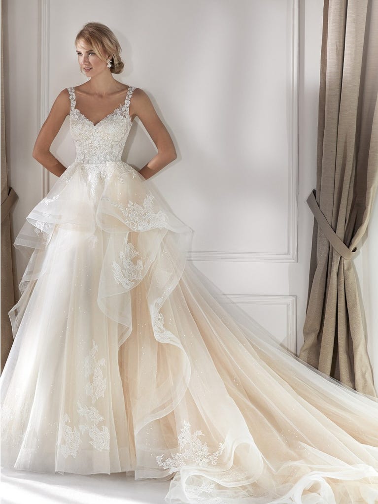 Romantic mermaid wedding dress of light pink Chantilly lace with plunging V-neck that continues on the sleeves. The keyhole opening in back and the tulle overskirt add romanticism to this dreamy dress.