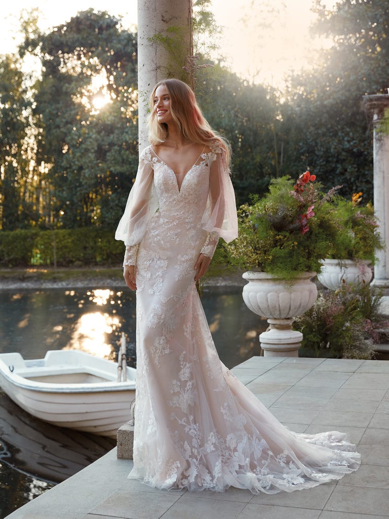 Flared wedding dress with crepe skirt and a tulle cape embroidered with silver beads. The three-dimensional flowers and minimalist, geometric superimpositions of fabrics create a contemporary, unique look for brides who want to surprise.